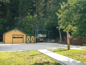 A yellow garage with a green roof, a covered outdoor area, and a tree in the foreground. - Wolf Creek FishHouse (Wolf Creek)