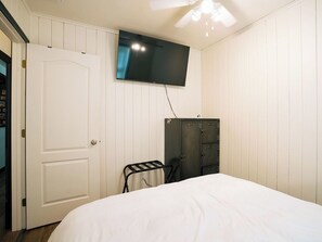 Une chambre à coucher avec un lit, une armoire, un téléviseur fixé au mur et une porte.