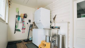 Ein Waschraum mit Waschmaschine, Spüle, Mülleimer und einem kleinen Holzhocker.