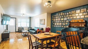 Ein Wohnzimmer mit einem Holzespeisetisch, Stühlen, einer Couch und einer Wand mit gerahmten Bildern.