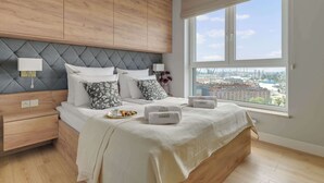 A modern bedroom with a large bed, wooden headboard, bedside lamps, and a city view.