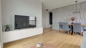 A modern living room with a flat-screen TV, a dining area with a table and chairs, and a wooden floor.