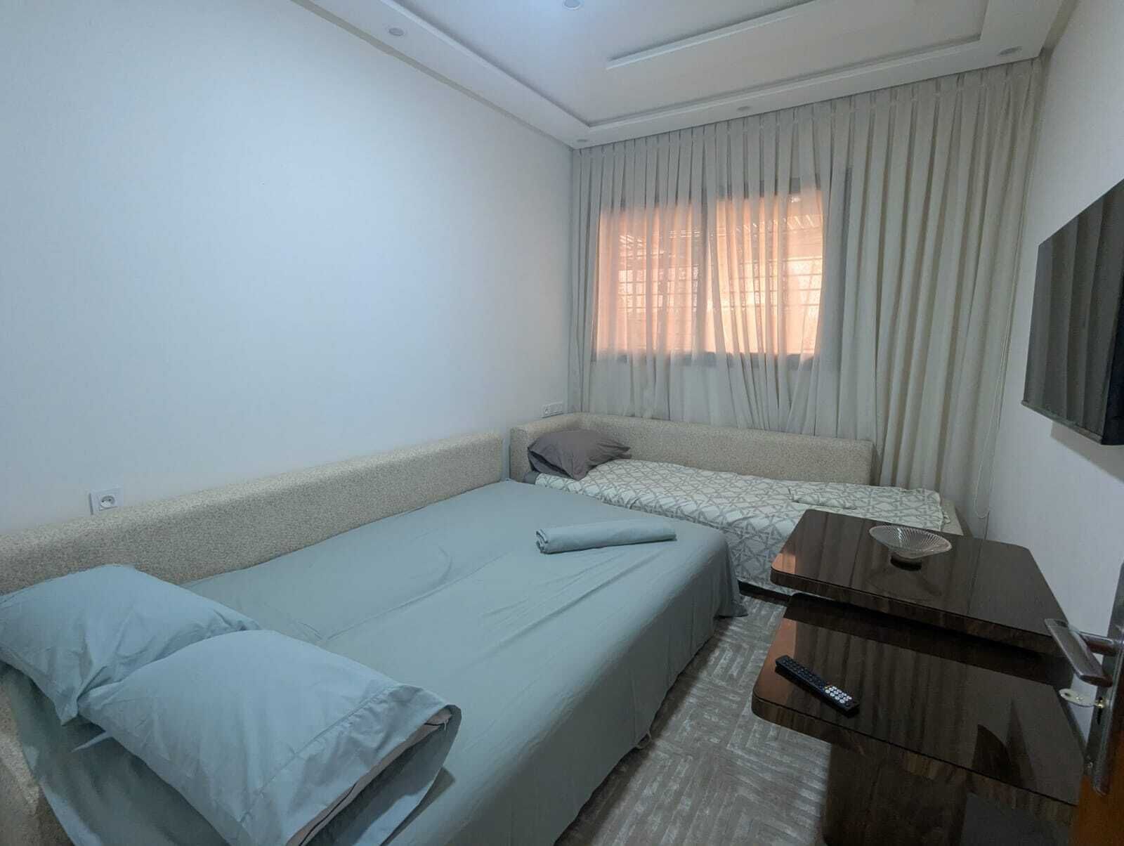 A small, simple room with two beds, a flat-screen TV, and a desk.