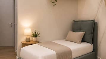 A bedroom with a bed, bedside table, lamp, and a wall-mounted shelf with a plant and picture.