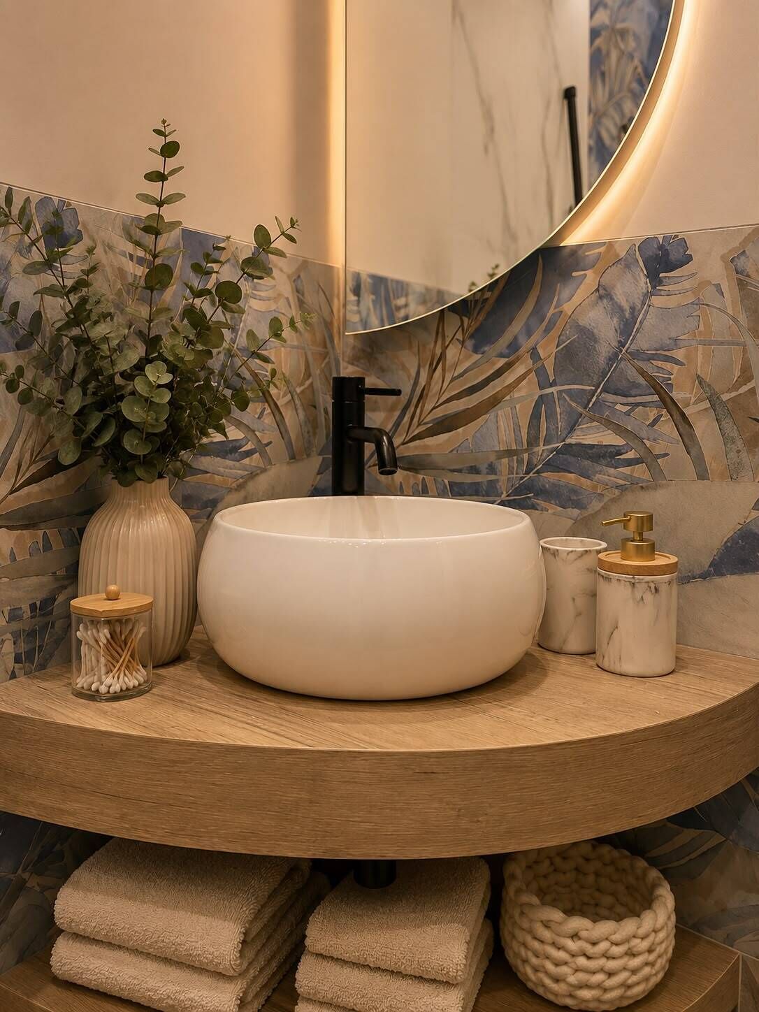 Un baño con un lavabo redondo, un espejo, una planta en maceta, un dispensador de jabón y toallas.