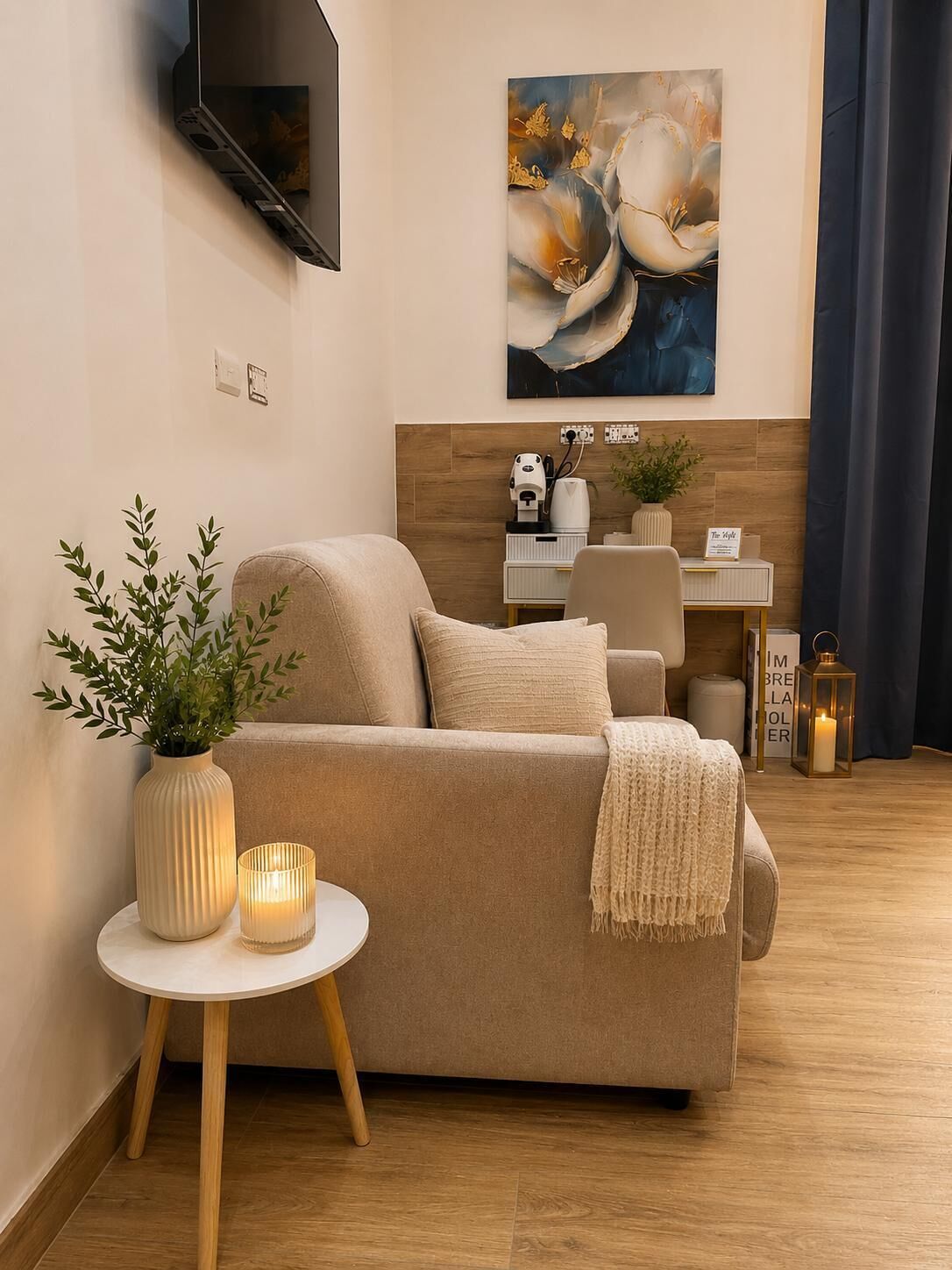 A living room with a beige sofa, a small table with a candle, a potted plant, and a painting on the wall.