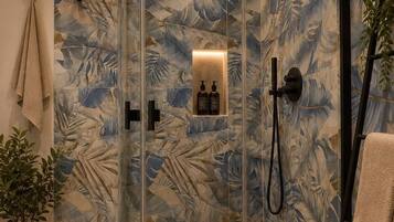 A modern shower enclosure with a glass door, a handheld showerhead, and a wall-mounted control panel.