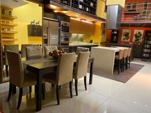 A modern kitchen with a dining area, featuring a large table and chairs, a fruit bowl, and a kitchen island with bar stools. - Sliema- Room in Historic Palazzo (Tas-Sliema)
