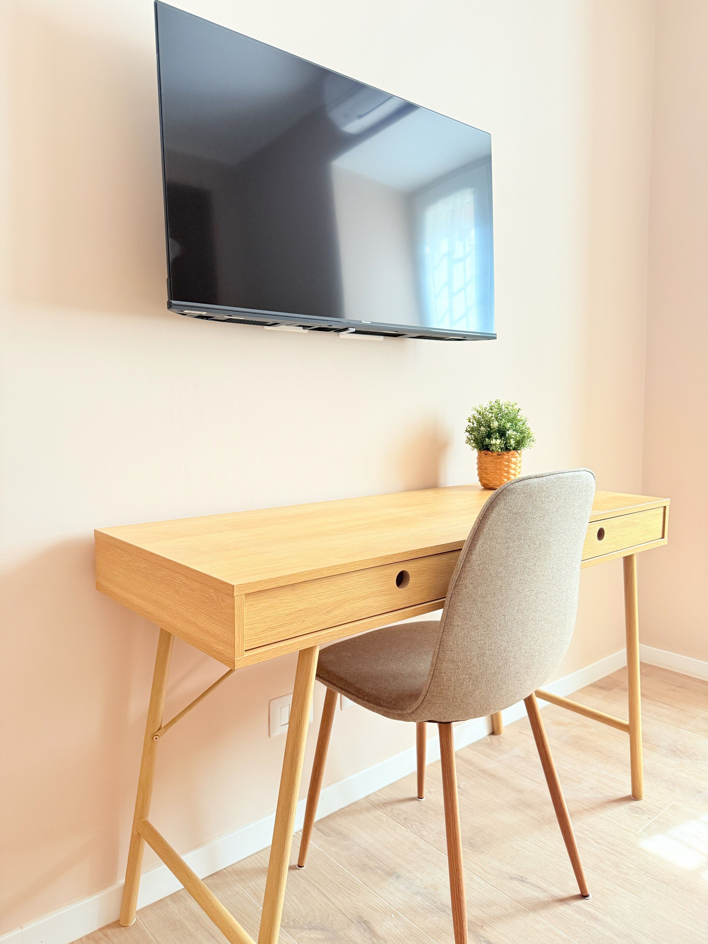Un bureau en bois avec un téléviseur fixé au-dessus, une chaise et une petite plante en pot posée sur le bureau.