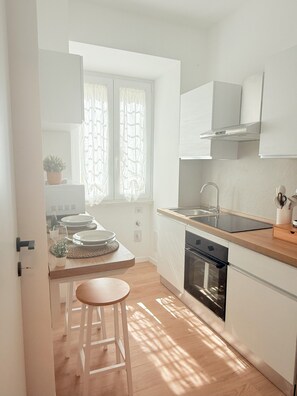 A modern kitchen with white cabinets, a wooden countertop, a sink, and a window with patterned curtains. - Santa Maria Apartment - Rome - 15 minutes from the Colosseum (Roma)