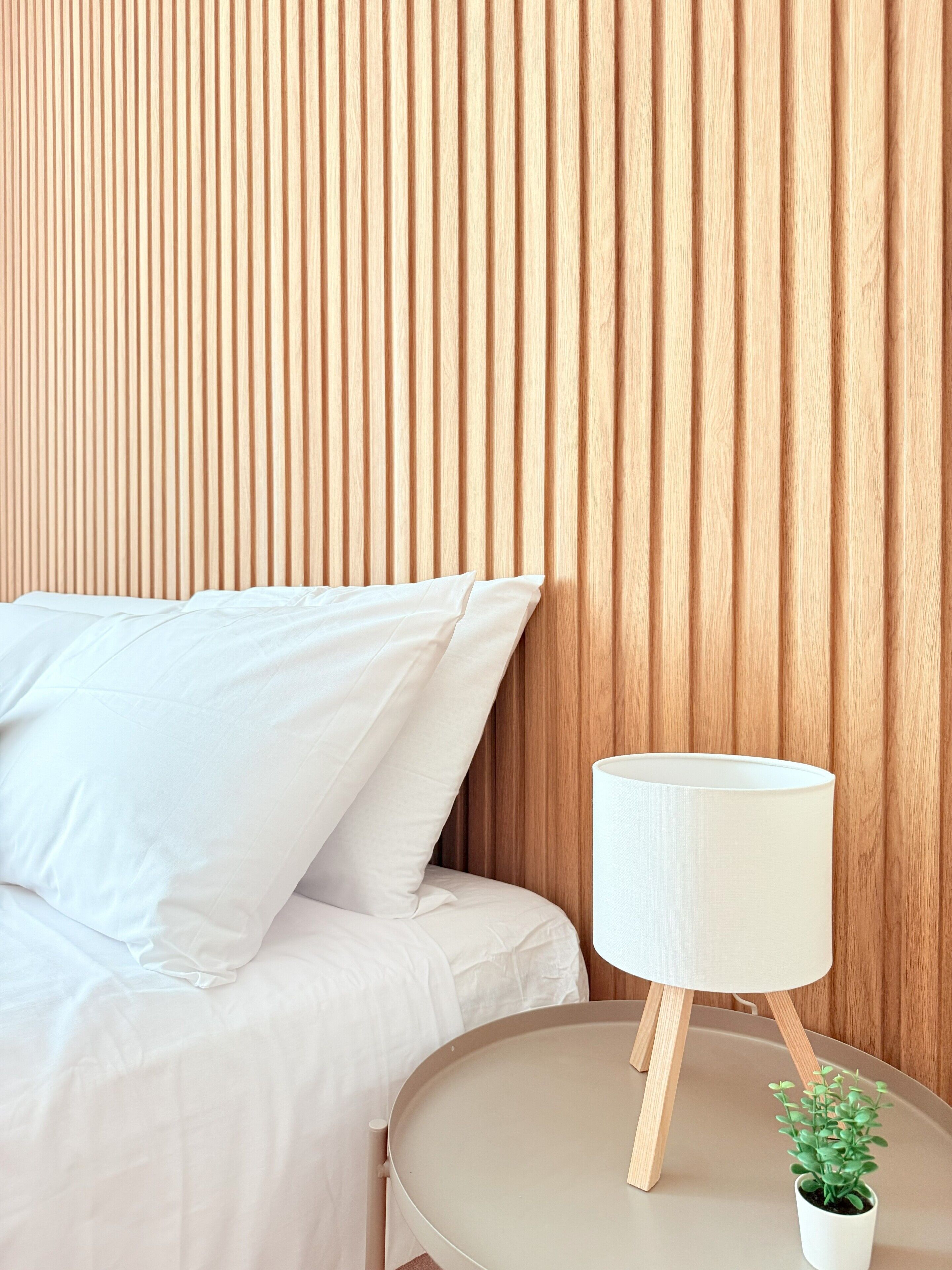 A bed with white bedding, a bedside table with a lamp, and a small potted plant.