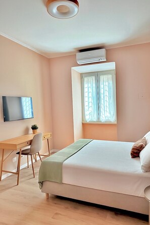 A bedroom with a bed, a desk, a chair, a television, and an air conditioning unit. - Santa Maria Apartment - Rome - 15 minutes from the Colosseum (Roma)