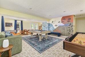 A room with a pool table, a sofa, a chair, a bookshelf, and a wall with a floral mural. - Perch&PineEscape, HotTub, Sauna, Firepit, Gameroom! (Basye)