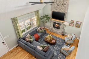 A living room with a stone fireplace, a large sofa, a coffee table, and a television. - Perch&PineEscape, HotTub, Sauna, Firepit, Gameroom! (Basye)