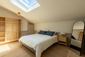 Ein Schlafzimmer mit Dachfenster, einem Bett mit weißer Bettwäsche, einem Nachttisch mit Lampe und einem großen Spiegel.