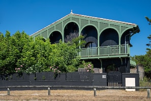 A building with a green facade, multiple arched windows, and a balcony. - La Pinède du Ferret - Climatisée et plage à 500 m (Lège-Cap-Ferret)