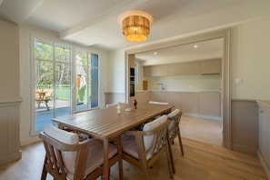 A dining area with a wooden table and chairs, a chandelier, and a view of a deck and trees. - La Pinède du Ferret - Climatisée et plage à 500 m (Lège-Cap-Ferret)