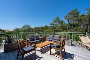 A wooden deck with outdoor furniture, including sofas and a table, surrounded by a green railing. - La Pinède du Ferret - Climatisée et plage à 500 m (Lège-Cap-Ferret)