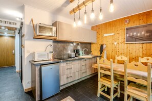 A compact kitchen with a microwave, toaster, and sink, wooden cabinets, and a dining area with benches. - Les Ambrunes - Station de ski accessible à pied (Châtel)