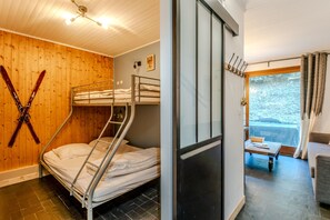 Une chambre avec des lits superposés, un porte-skis, une porte coulissante donnant sur un balcon et une vue sur un paysage enneigé.
