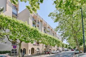 A multi-story building with balconies, a no parking sign, and parked cars along the street. - Studio Z - Parc des Expos (Vanves)