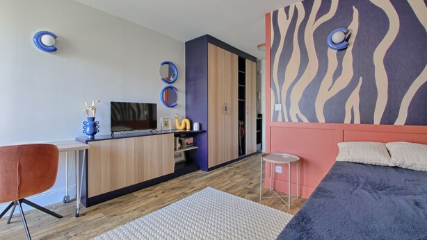 Een moderne slaapkamer met een bed, bureau, stoel, televisie en een garderobe.