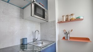 Een keuken met een roestvrijstalen spoelbak, een magnetron en een plank met potten en keukengerei.
