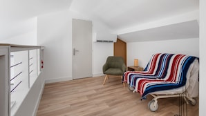 Ein Zimmer mit Holzboden, einem grünen Sessel, einem Nachttisch mit Lampe, einer gestreiften Decke und einer weißen Tür.