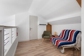 Ein Zimmer mit Holzboden, einem grünen Sessel, einem Nachttisch mit Lampe, einer gestreiften Decke und einer weißen Tür.