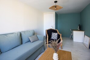 A living room with a light blue sofa, a wooden coffee table with a vase, a black and white chair, and a white cabinet. - Villa Trafal - Proche plage (Saint-Michel-en-l'Herm)