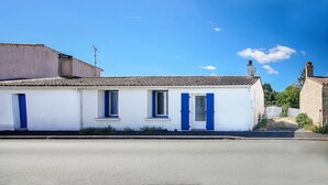 Ein weißes Gebäude mit blauen Fensterläden und einem Ziegeldach unter blauem Himmel.