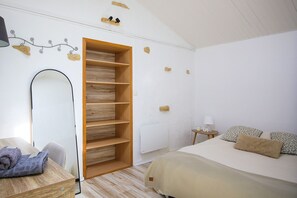 A bedroom with a bed, a wooden wardrobe, a mirror, a small bedside table with a lamp, and a wall with a light fixture. - Villa Trafal - Proche plage (Saint-Michel-en-l'Herm)