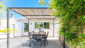 Eine Terrasse im Freien mit Tisch und Stühlen, einer Pergola und Blick auf ein Haus.