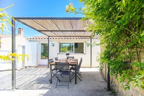 An outdoor patio with a table and chairs, a pergola, and a view of a house. - Villa Trafal - Proche plage (Saint-Michel-en-l'Herm)