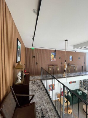 A modern interior with wooden paneling, a glass railing, and a seating area with a green sofa and round tables. - Casa de Santo António - Suite 1 (Marco de Canaveses)