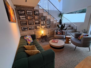A modern living room with a green sofa, armchairs, a coffee table, and a staircase leading to an upper level.