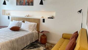 Une chambre d’hôtel avec un lit, un canapé, un tapis, un tableau et des lampes fixées au mur.