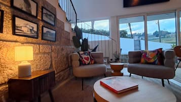 Ein modernes Wohnzimmer mit Steinwand, einer Treppe und Blick auf ein Gewässer.