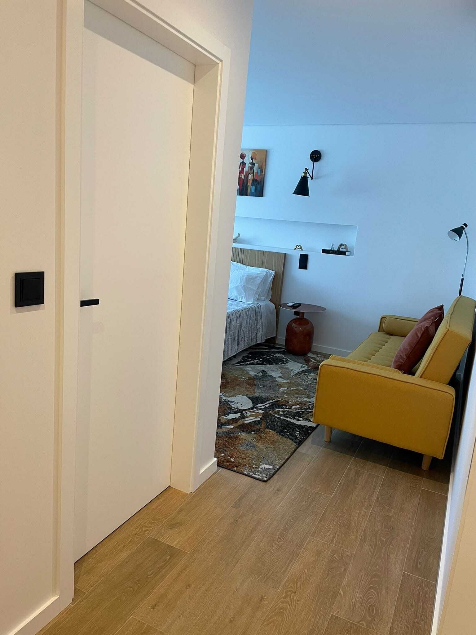 Et værelse med en seng, en gul sofa, et lille bord og et tæppe.