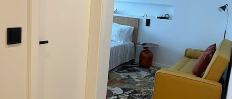 Una habitación con una cama, un sofá amarillo, una mesita y una alfombra.