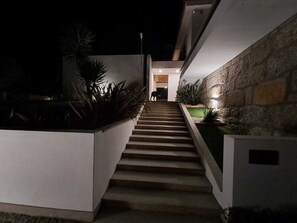 A nighttime view of a modern staircase leading to a building entrance, surrounded by plants and stone walls. - Casa de Santo António - Suite 1 (Marco de Canaveses)
