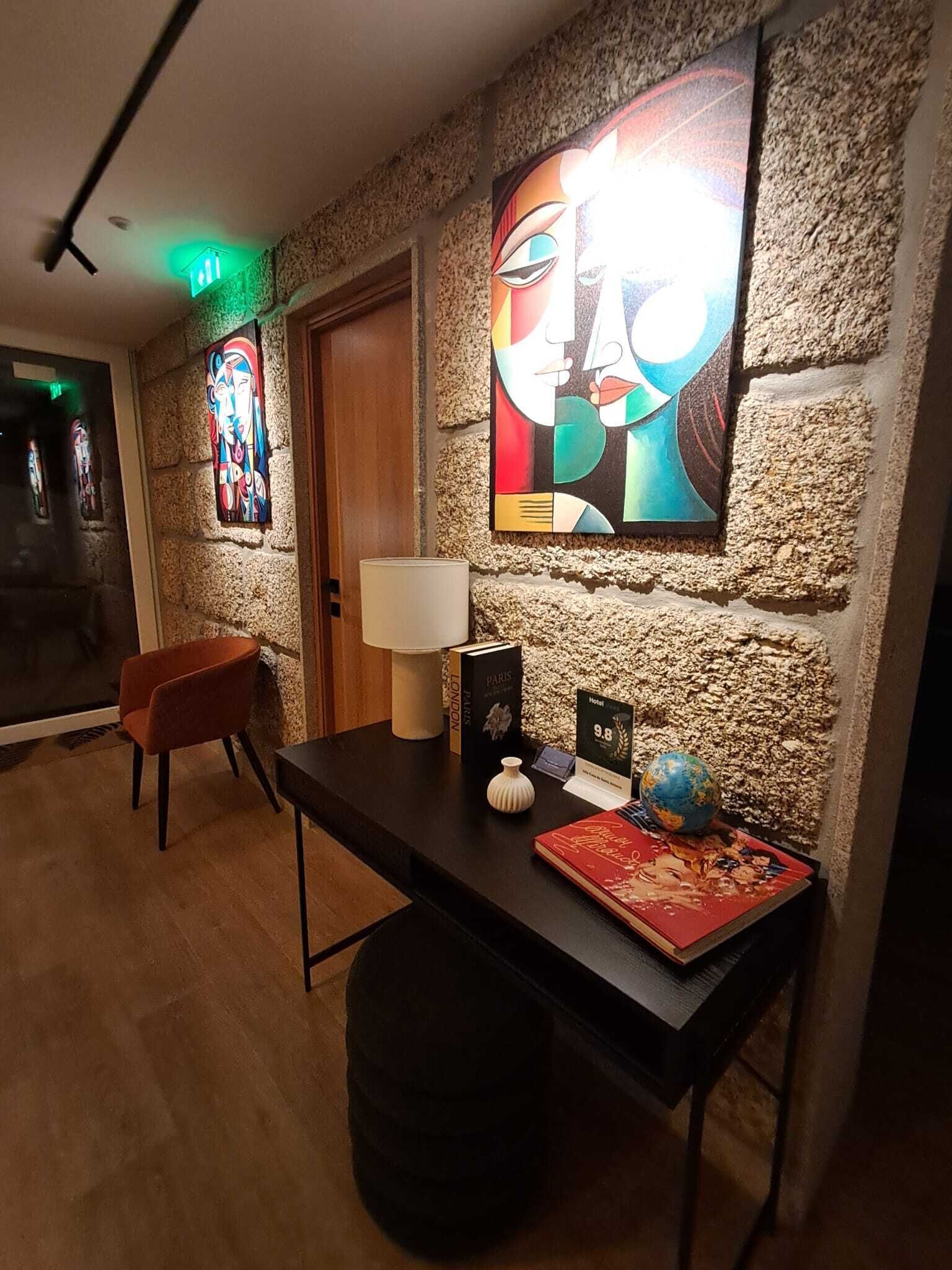 En hotellobby med en stenvæg, et stort abstrakt maleri, en trædør, et skrivebord med en globus, en lampe og en stol.