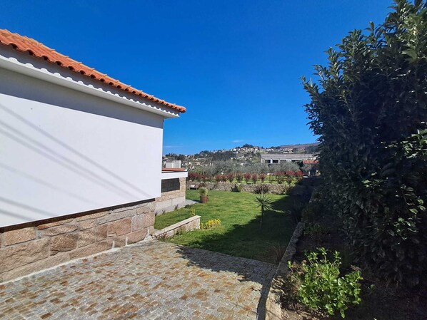 A residential property with a paved driveway, a white building with a red-tiled roof, and a well-maintained garden.