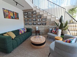 A modern living room with a green sofa, a grey armchair, a round wooden coffee table, and a staircase with a stone wall.