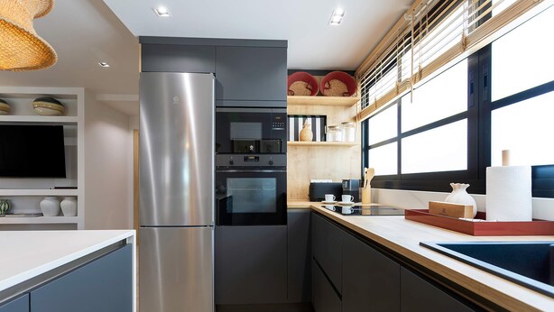 Eine moderne Küche mit einem Edelstahl-Kühlschrank, einem Einbauofen und einer Mikrowelle. Es gibt ein Holzregal mit Gläsern und einem Korb, sowie ein Fenster, das natürliches Licht hereinlässt.