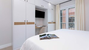 Ein Hotelzimmer mit Bett, Kleiderschrank, Flachbildfernseher und einem Fenster mit Vorhängen.