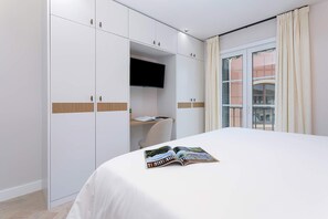 Ein Hotelzimmer mit Bett, Kleiderschrank, Flachbildfernseher und einem Fenster mit Vorhängen.