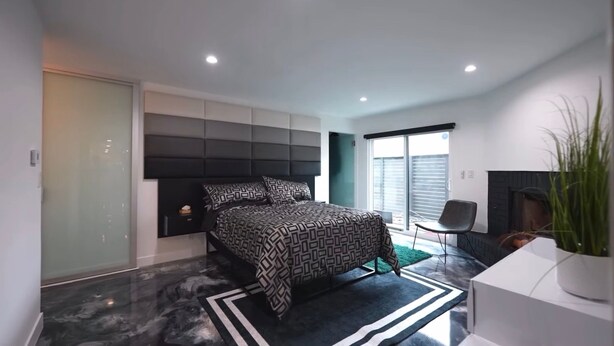 Un dormitorio moderno con cama, una puerta corredera, una silla y una planta.
