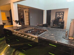 Une cuisine moderne dotée d’un grand îlot central, de meubles de couleur noire et d’une hotte de cuisson en acier inoxydable.