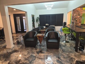 A modern dining area with a marble floor, black leather chairs, a bar with green stools, and a large window with blinds. - Spacious private Oasis (Los Angeles)